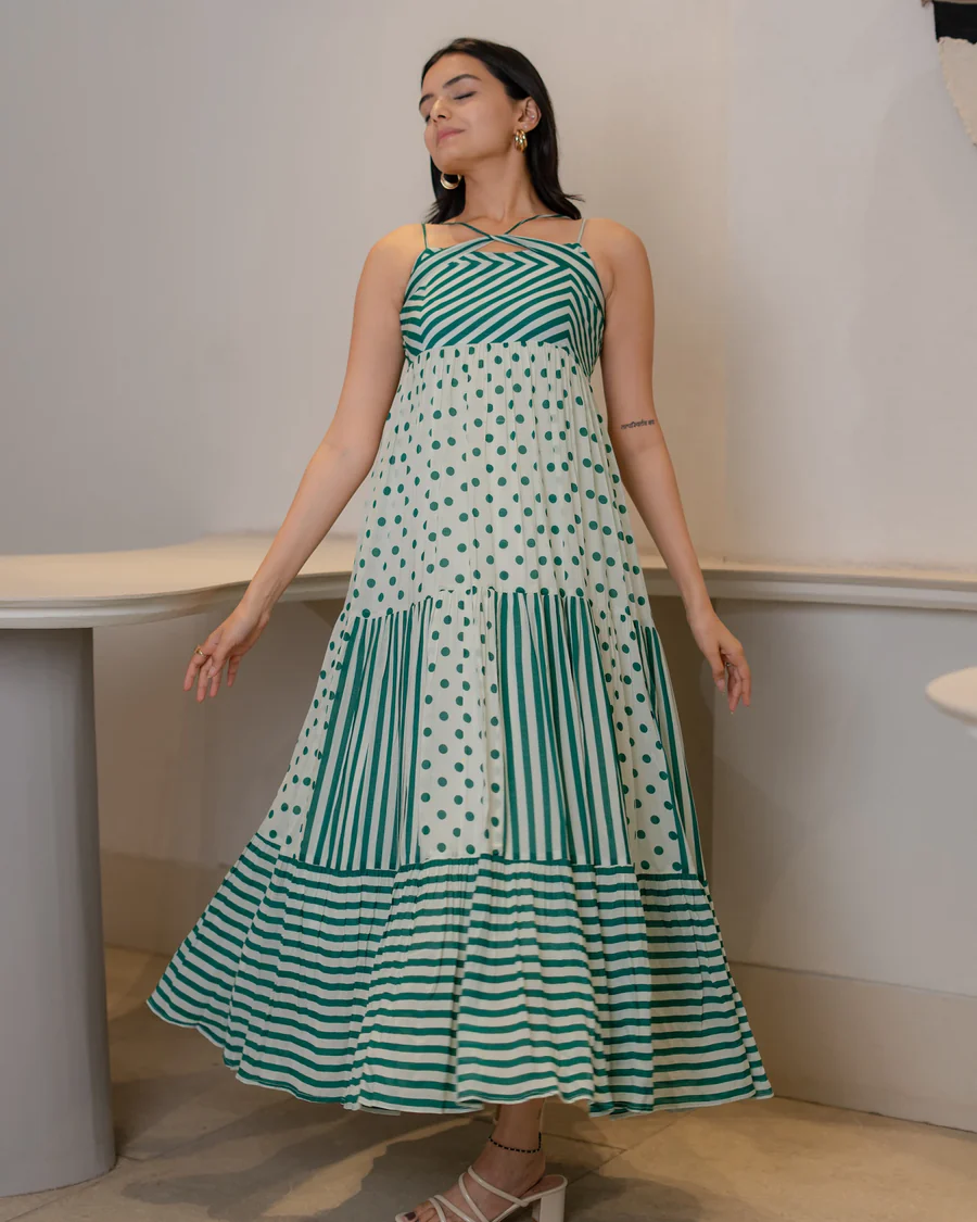 Woman wearing sleeveless green and white maxi dress with polka dot and stripe patterns, posing indoors.