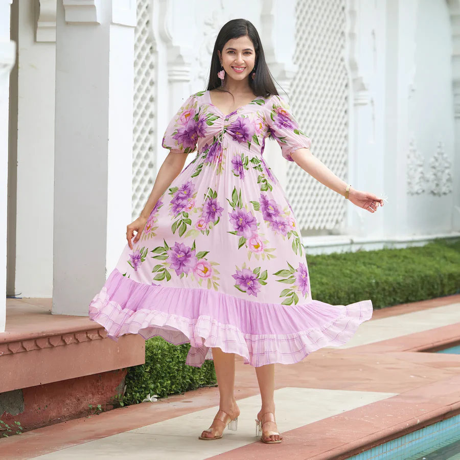 Woman in pink floral dress with puff sleeves and ruffle hem posing near a white architectural wall.